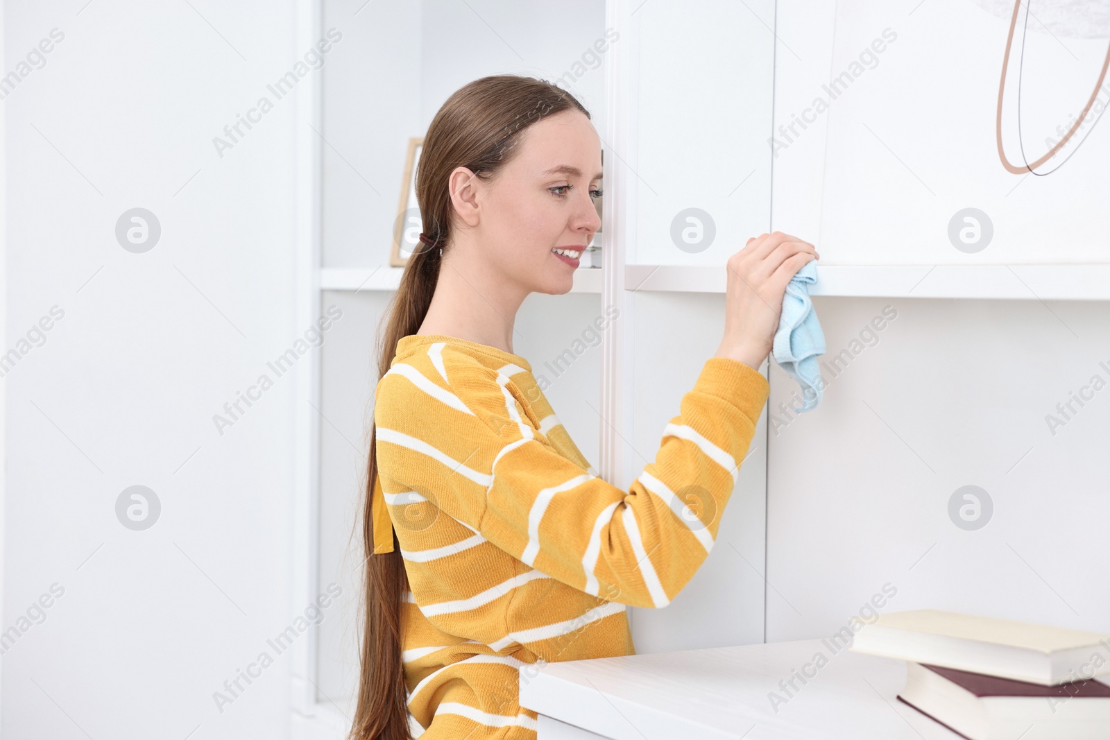 Photo of Woman cleaning shelf with rag at home