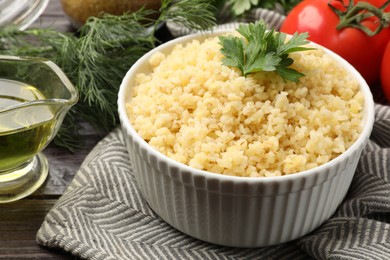 Delicious bulgur with parsley in bowl and products on table, closeup