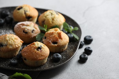 Photo of Delicious muffins with powdered sugar, blueberries and mint on light grey table, closeup