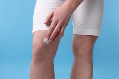 Man applying ointment onto his knee on light blue background, closeup