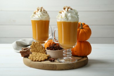 Photo of Tasty pumpkin latte with whipped cream in glasses, spices and cookies on white wooden table