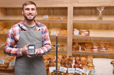 Photo of Smiling seller holding payment terminal in bakery. Space for text