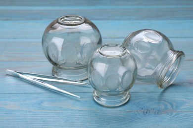 Photo of Glass cups and tweezers on light blue wooden table, closeup. Cupping therapy