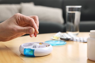 Photo of Woman with pills and organizer at light wooden table, closeup