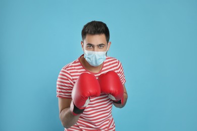 Man with protective mask and boxing gloves on light blue background. Strong immunity concept