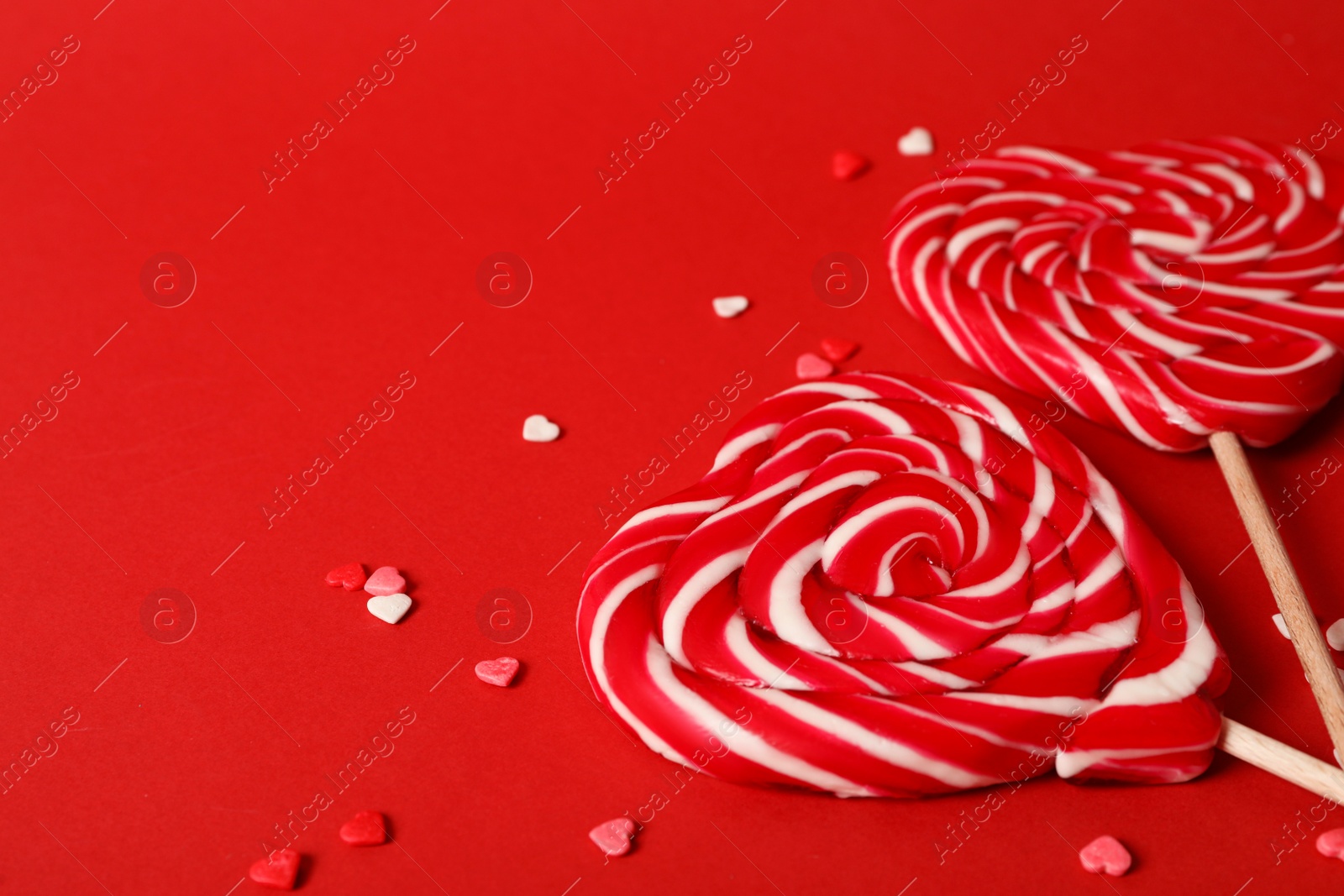 Photo of Sweet heart shaped lollipops and sprinkles on red background, closeup view with space for text. Valentine's day celebration