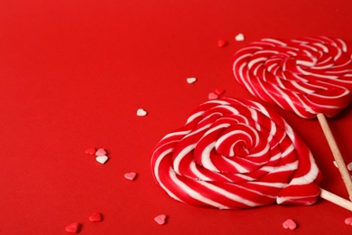 Photo of Sweet heart shaped lollipops and sprinkles on red background, closeup view with space for text. Valentine's day celebration