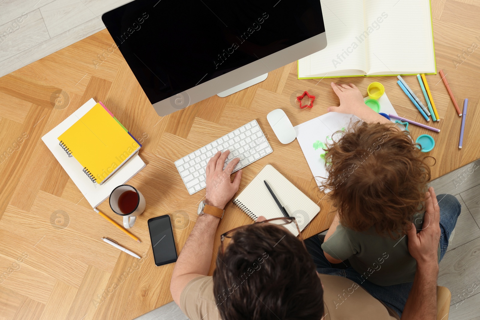 Photo of Man working remotely at home. Father and his son at desk with computer, top view