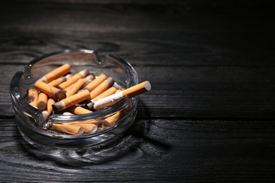 Photo of Glass ashtray with cigarette stubs on black wooden table