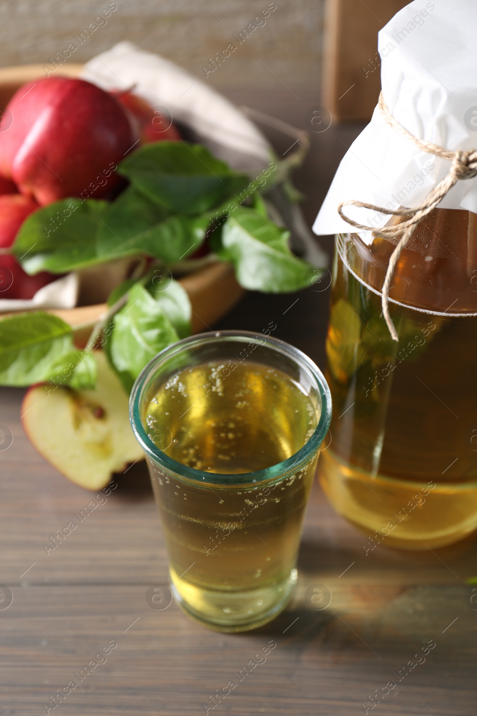 Photo of Delicious cider, red apples and green leaves on wooden table, closeup