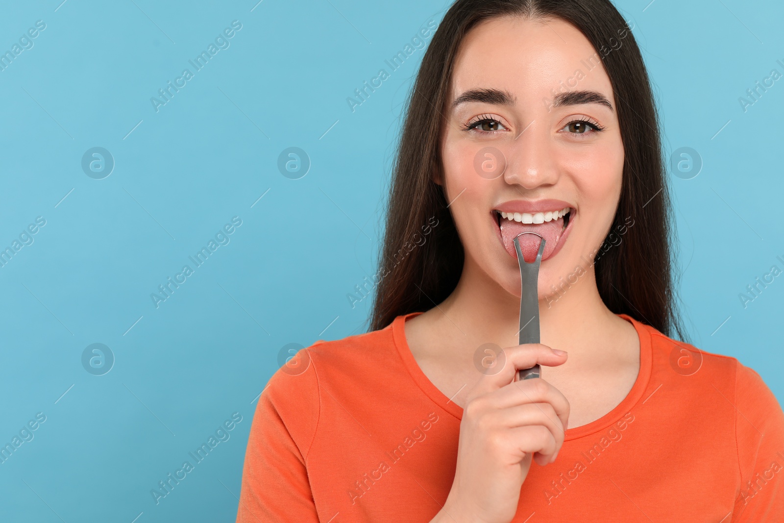 Photo of Happy woman brushing her tongue with cleaner on light blue background, space for text