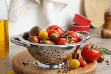 Metal colander with fresh tomatoes on wooden table