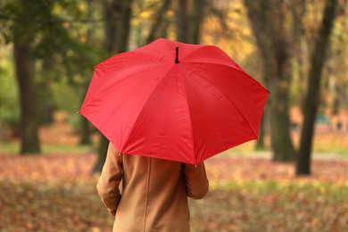 Photo of Woman with red umbrella walking in autumn park, back view