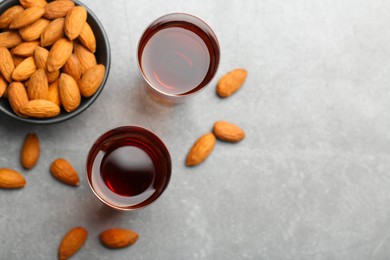 Glasses with tasty amaretto liqueur and almonds on gray table, flat lay. Space for text