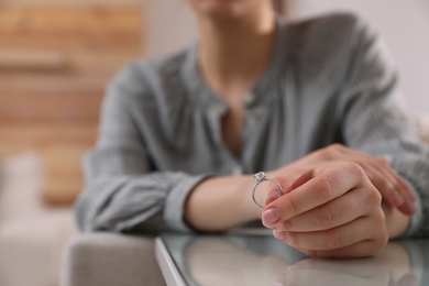 Photo of Woman holding wedding ring at table indoors, space for text. Divorce concept