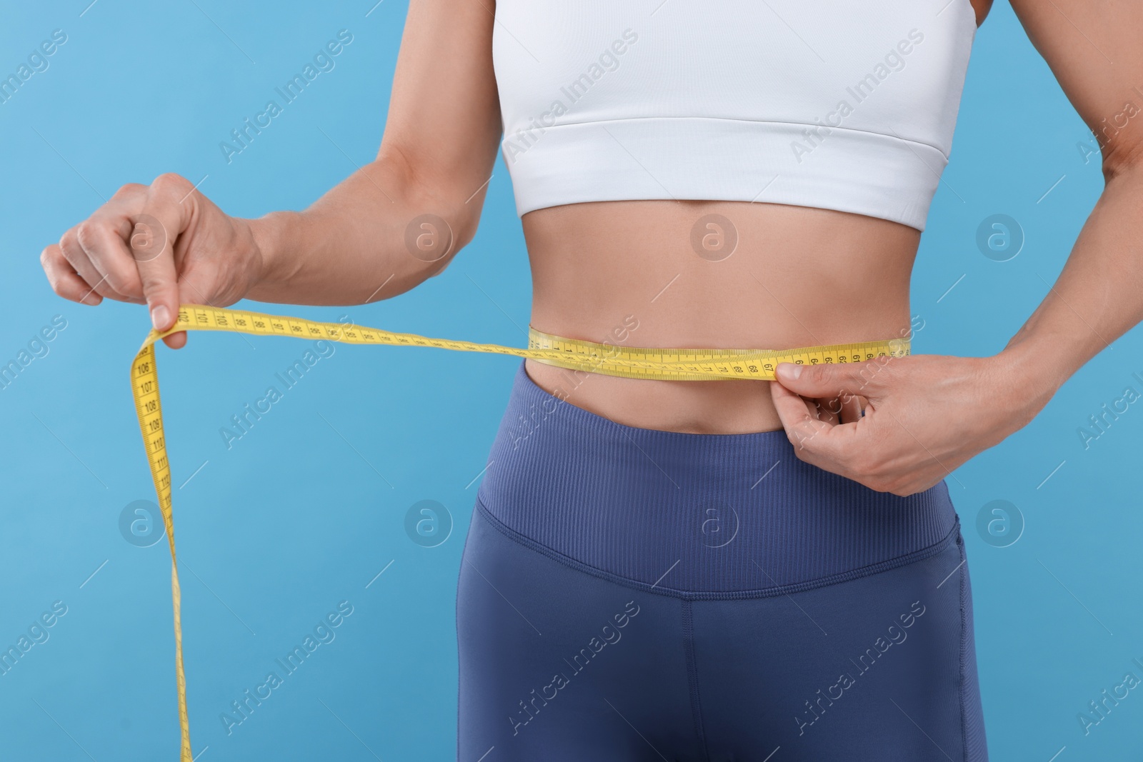 Photo of Slim woman measuring waist with tape on light blue background, closeup. Weight loss