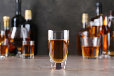 One liqueur in glass in front of others on grey textured table, closeup