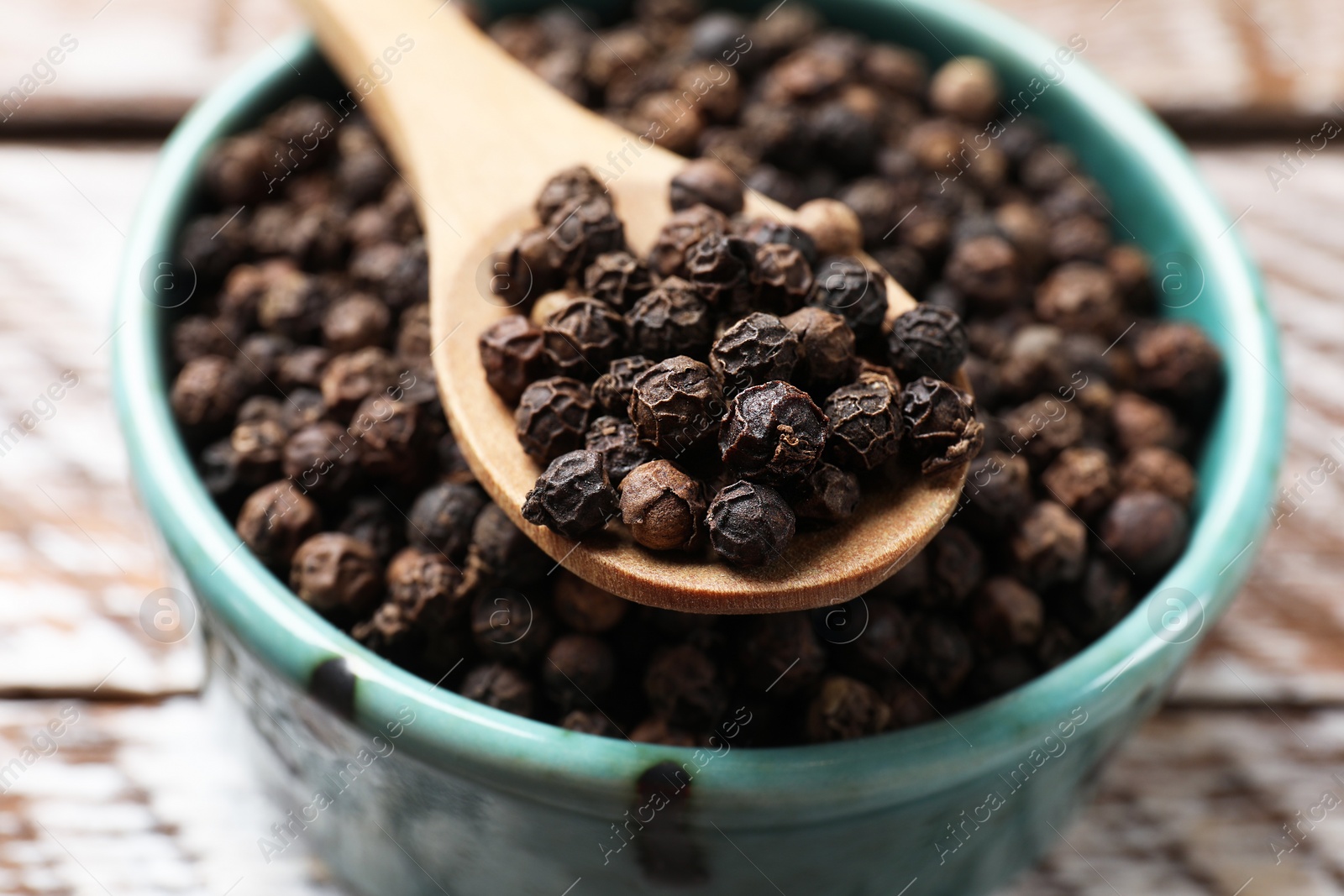 Photo of Aromatic spice. Black pepper in bowl and spoon on wooden table, closeup