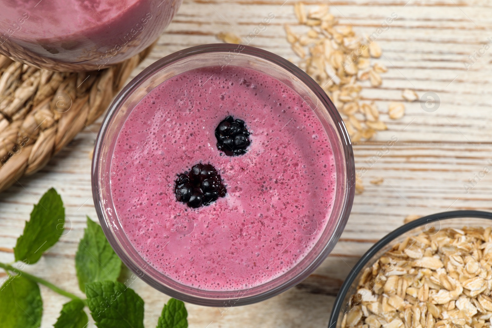 Photo of Glass of blackberry smoothie with mint and oatmeal on light wooden table, flat lay