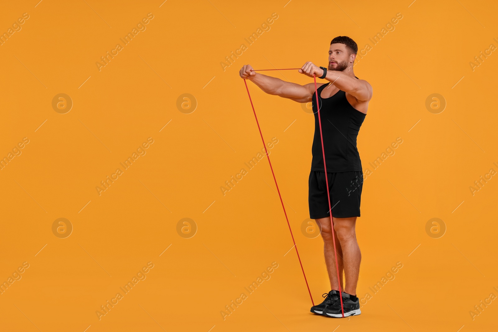 Photo of Young man exercising with elastic resistance band on orange background. Space for text