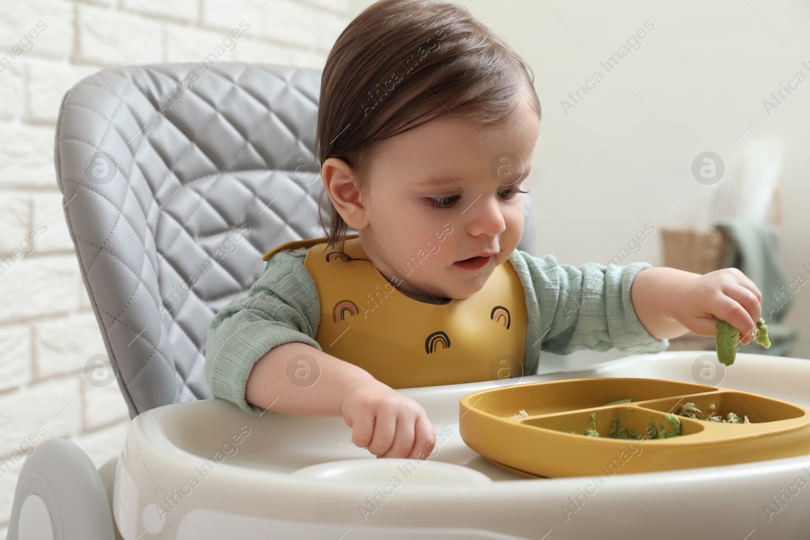 Photo of Cute little baby eating healthy food in high chair indoors