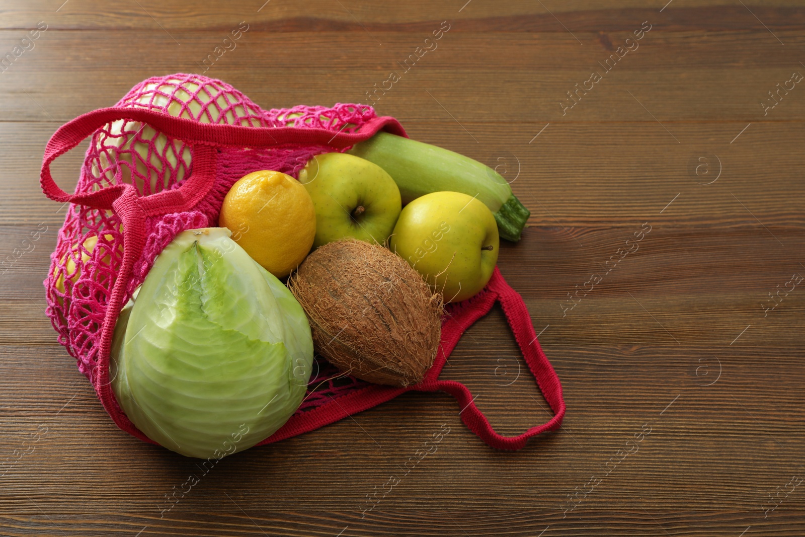 Photo of Net bag with vegetables and fruits on wooden table