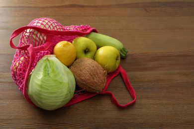 Net bag with vegetables and fruits on wooden table