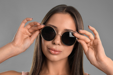 Beautiful young woman wearing sunglasses on grey background, closeup