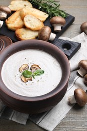 Photo of Delicious homemade mushroom soup in ceramic pot and fresh ingredients on wooden table