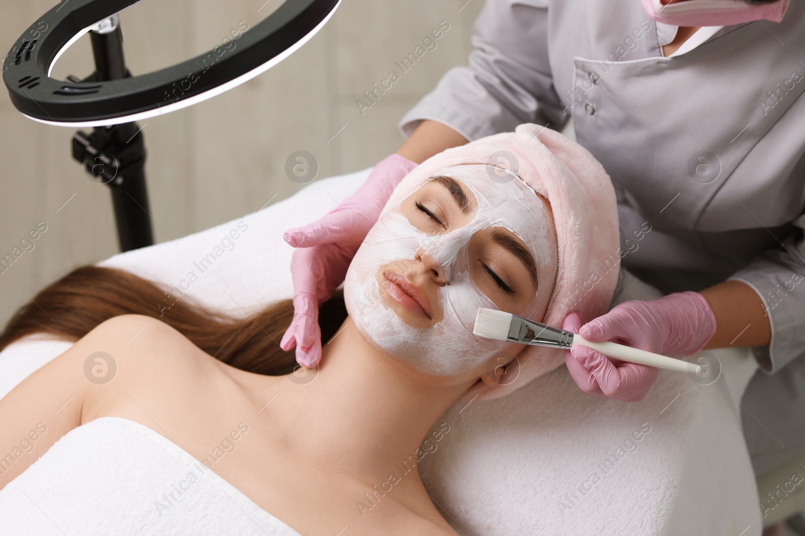 Photo of Cosmetologist applying mask on woman's face in clinic, top view