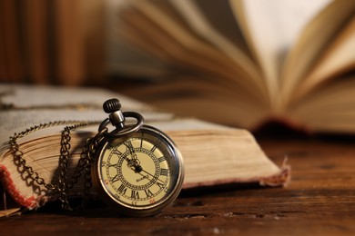 Pocket clock with chain and book on wooden table, closeup. Space for text