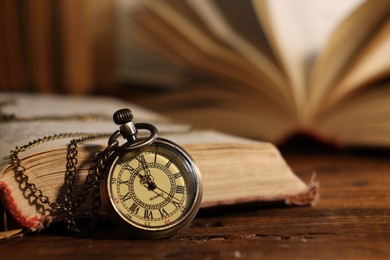 Photo of Pocket clock with chain and book on wooden table, closeup. Space for text