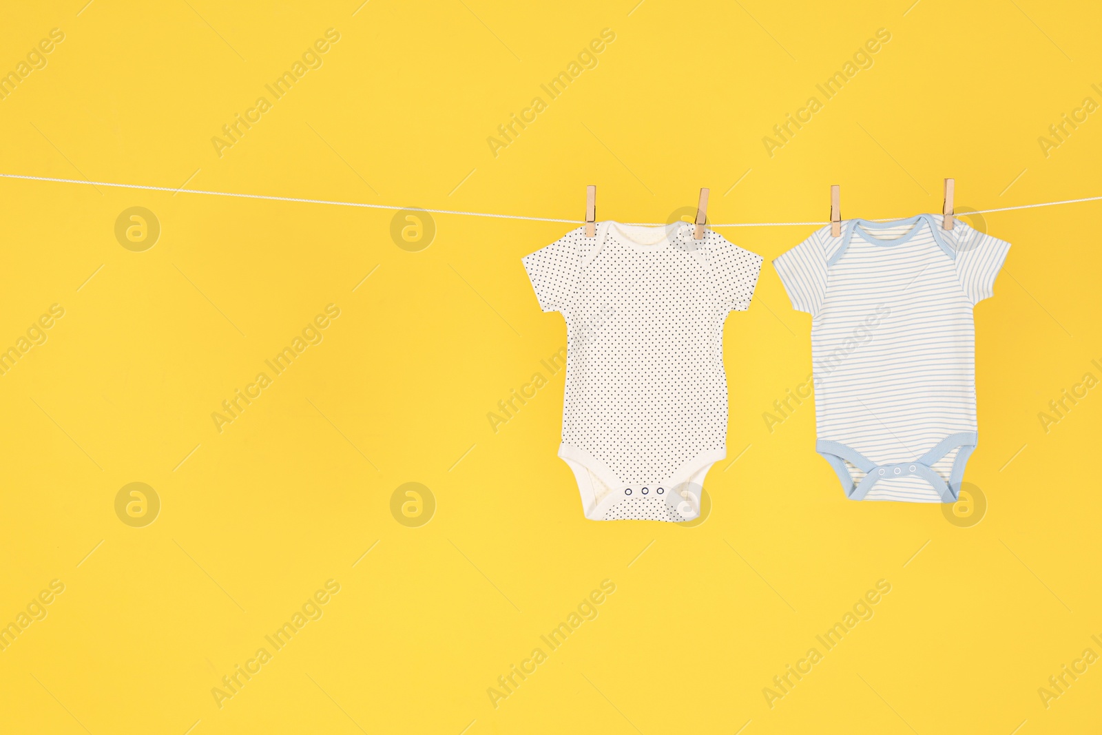 Photo of Baby onesies hanging on clothes line against yellow background, space for text