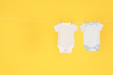 Photo of Baby onesies hanging on clothes line against yellow background, space for text