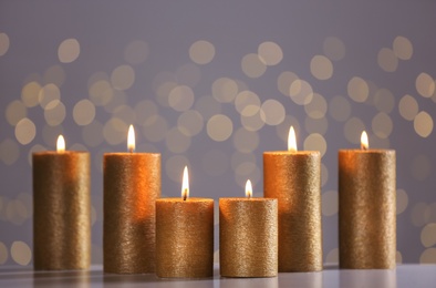 Photo of Burning gold candles on table against blurred lights. Space for text