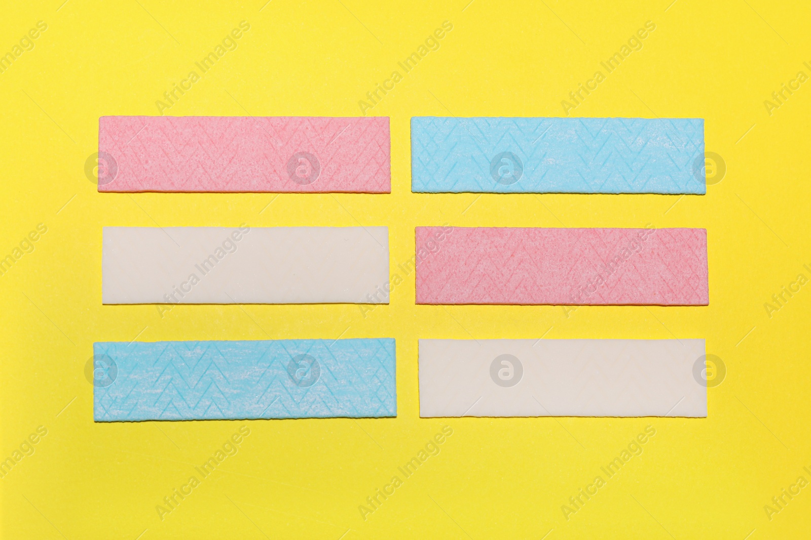 Photo of Sticks of tasty chewing gum on yellow background, flat lay