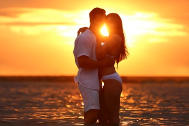 Happy young couple spending time together on sea beach at sunset