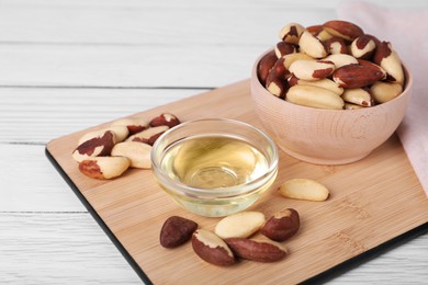 Photo of Tasty Brazil nuts and oil on white wooden table