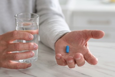Photo of Senior man with pill and glass of water at table on blurred background, closeup