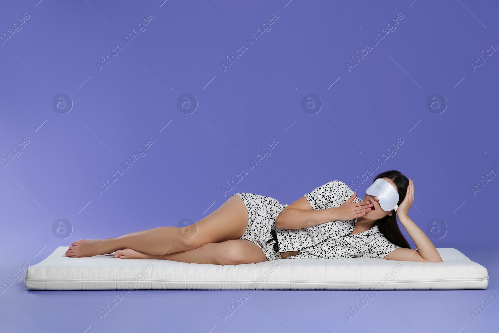 Photo of Woman with sleep mask lying on soft mattress against light purple background