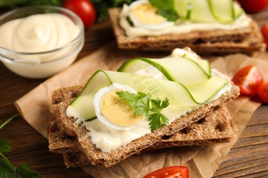 Photo of Fresh rye crispbreads with quail egg, cream cheese and cucumber slices on wooden table, closeup