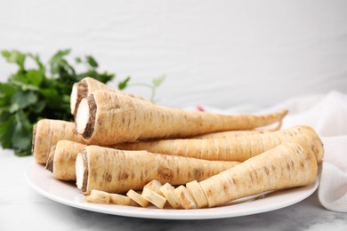 Plate with whole and cut parsley roots on white table, closeup