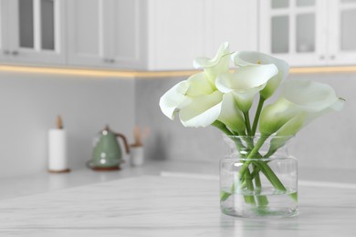 Photo of Glass vase with beautiful calla lily flowers on table in kitchen. Space for text
