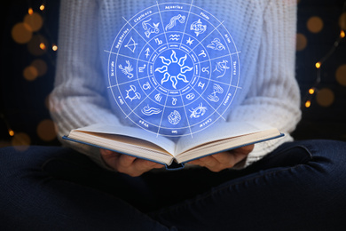Young woman reading book at home and illustration of zodiac wheel with astrological signs