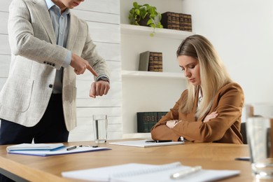 Businessman pointing on wrist watch while scolding employee for being late in office