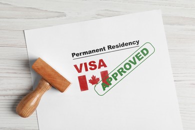 Image of Document with approved permanent residency visa in Canada and stamp on white wooden table, top view