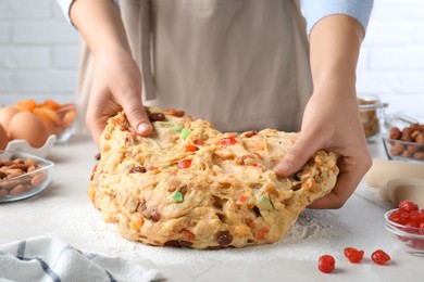 Photo of Woman kneading dough with candied fruits and nuts for Stollen at white table, closeup. Baking traditional German Christmas bread