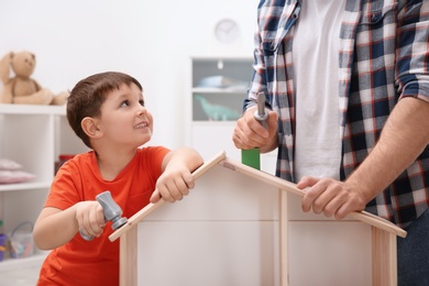 Man and his child playing builders with wooden doll house at home