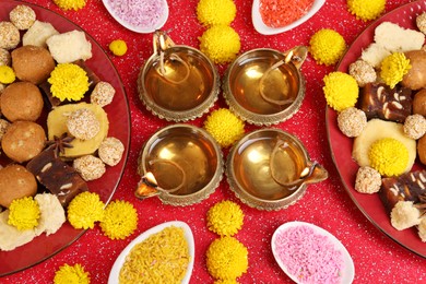 Photo of Diwali celebration. Flat lay composition with diya lamps and tasty Indian sweets on shiny red table