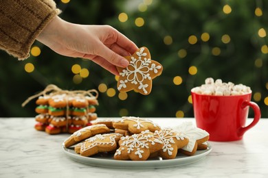 Photo of Woman with decorated cookie at table against blurred Christmas lights, closeup